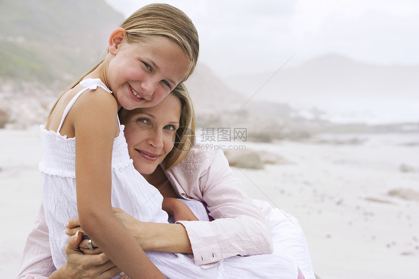在海滩上拥抱小女儿的快乐女人的肖像图片