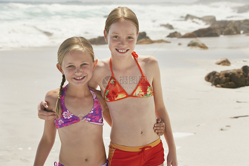 快乐的小姐妹们的肖像 站在海滩上手抱双臂图片