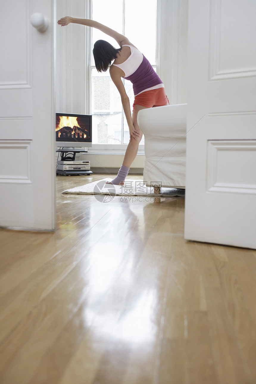 一位年轻妇女在客厅内锻炼和看电视的后视镜图片