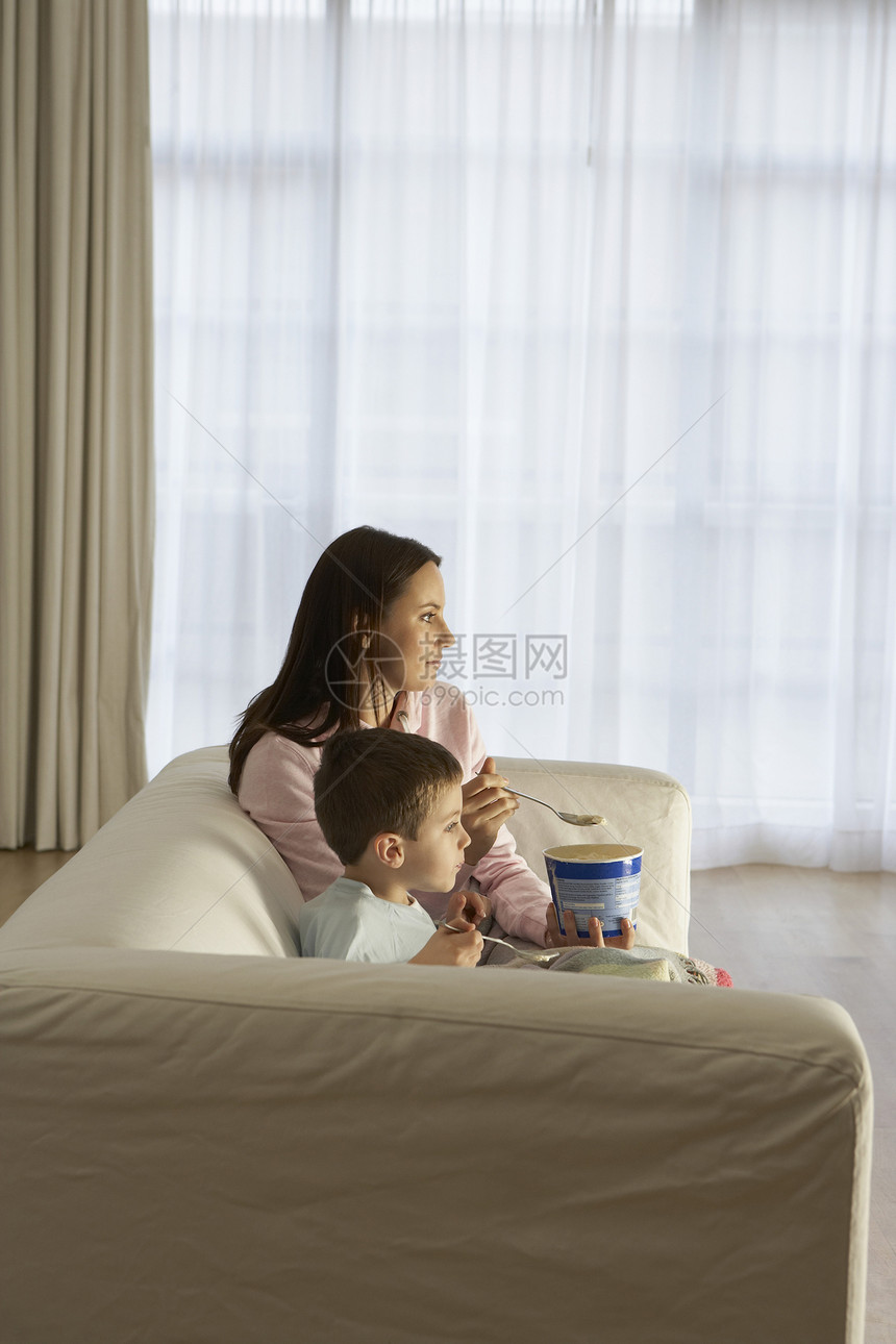 母亲和儿子在家吃冰淇淋时观看电视的侧面观图片