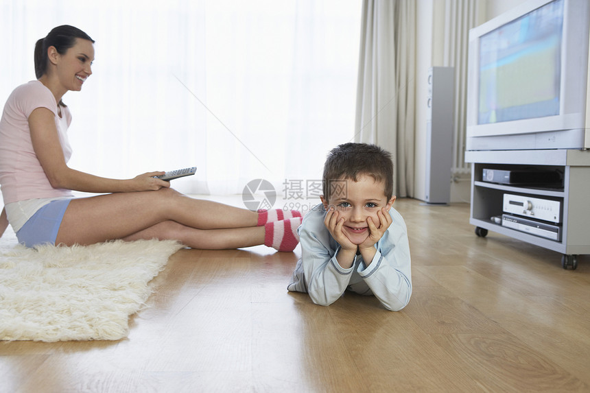 坐在地板上 看她儿子的电视的年轻女子图片