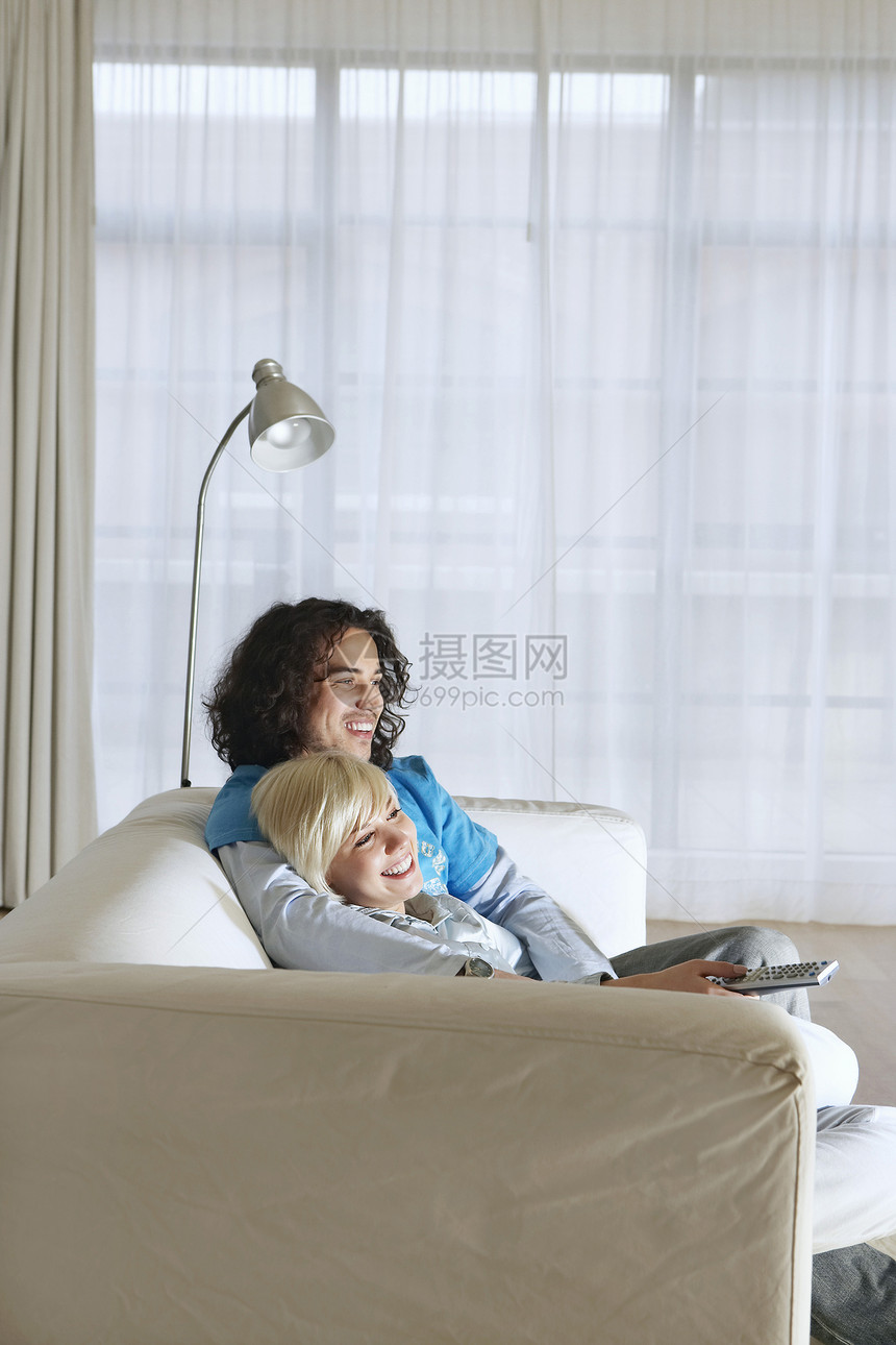 坐在沙发上看电视的一对快乐情侣的侧边景色图片
