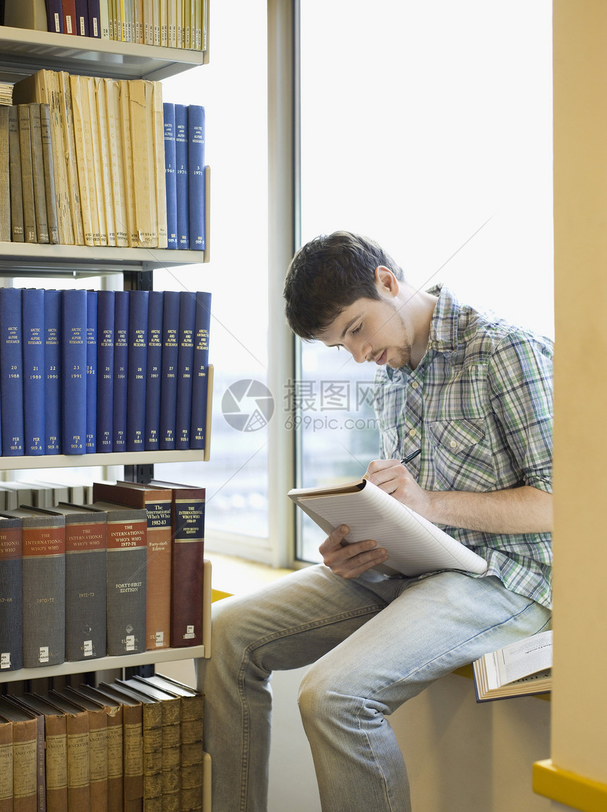 坐在图书馆和书写笔记窗边的男青年学生图片