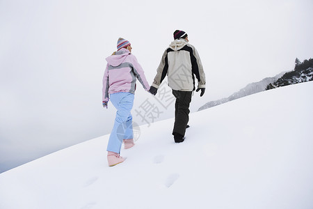 一对在雪覆盖的山丘上行走的夫妇 后仰低角视图丘陵女性女士中年人团结男人中年男子成人服装背景图片