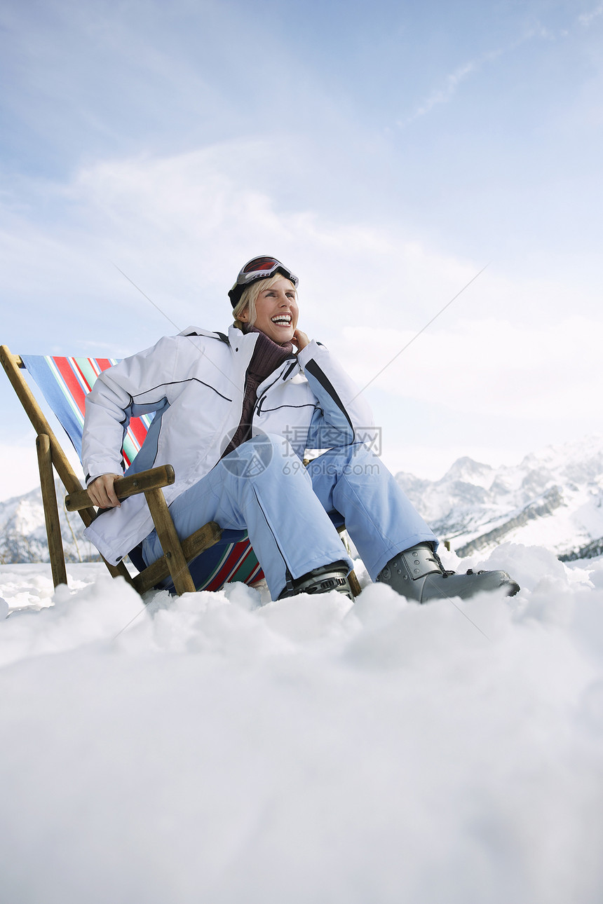 在雪山上坐在甲板椅上的 微笑着的女人的低角度视角图片