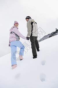 一对在雪覆盖的山丘上行走的夫妇 后仰低角视图微笑两个人成人团结活动女性快乐滑雪服夫妻女士背景图片