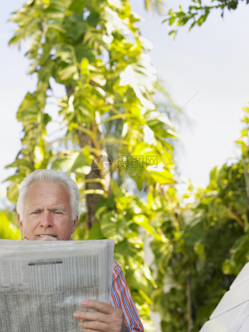 轻松的成熟男子阅读报纸反对户外种植植物图片