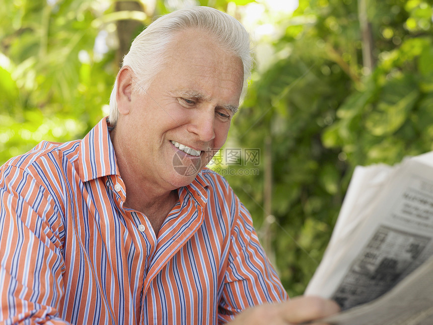 一个笑着的成熟男子在户外阅读报纸时图片