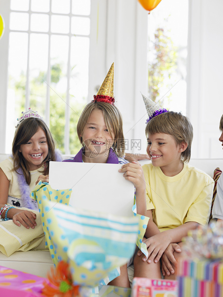 三个孩子在生日派对上 一个打开礼物幸福男生朋友们快乐孩子们闲暇青春期友谊皇冠展示图片