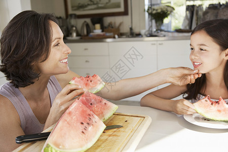 坐着西瓜的孩子幸福的母亲和女儿在厨房桌边吃西瓜背景