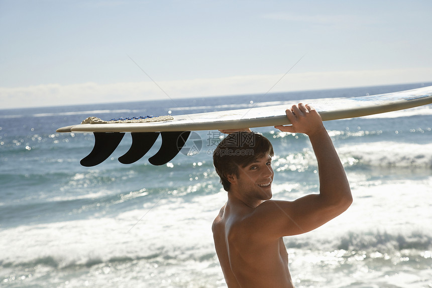 英俊年轻男子的肖像 他携带冲浪船在海边图片