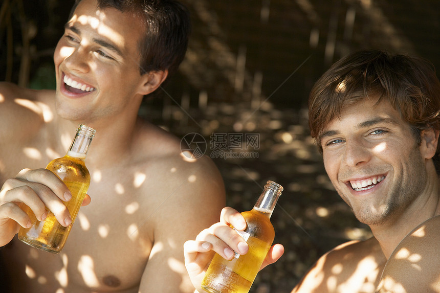 带着朋友在户外喝啤酒的微笑的年轻男人的肖像图片