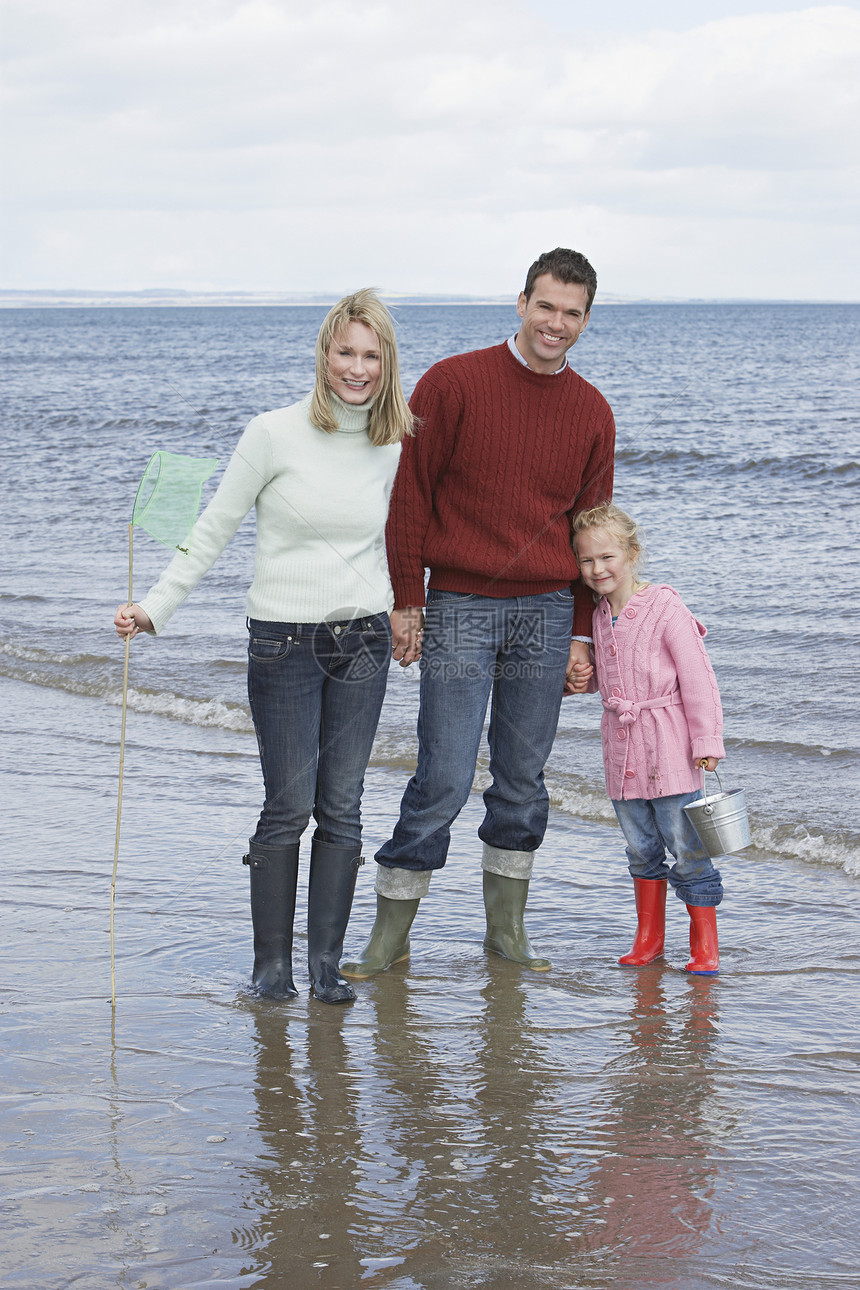 快乐父母的肖像 女儿在海滩上拿着渔网和水桶图片