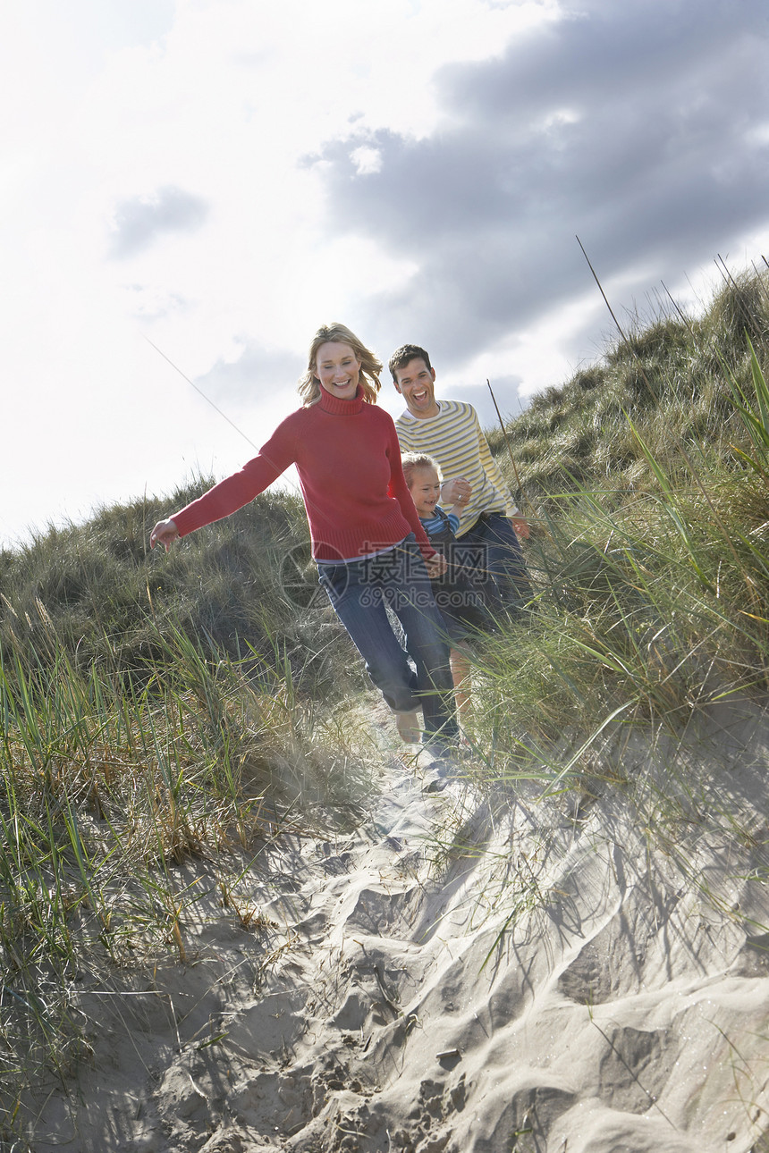 整个父母和女儿在海滩上穿过沙丘跑遍沙滩图片
