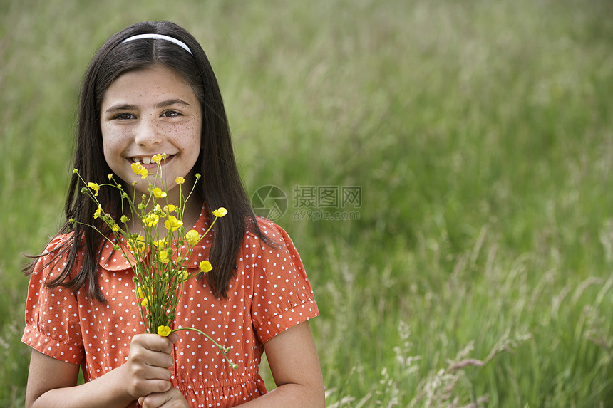 快乐的年轻女孩在田里拿着一束鲜花的肖像图片