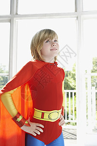 做自己的英雄穿着超级英雄服装的金发小男孩 站在室内臀部举起手来背景
