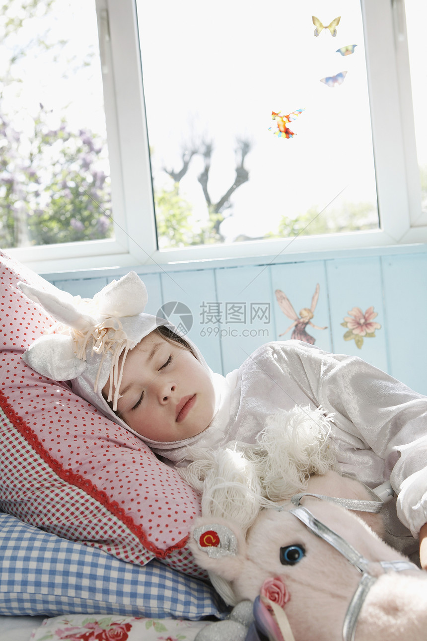 穿着独角兽服装的年轻女孩睡在床上 带着玩具马睡觉图片
