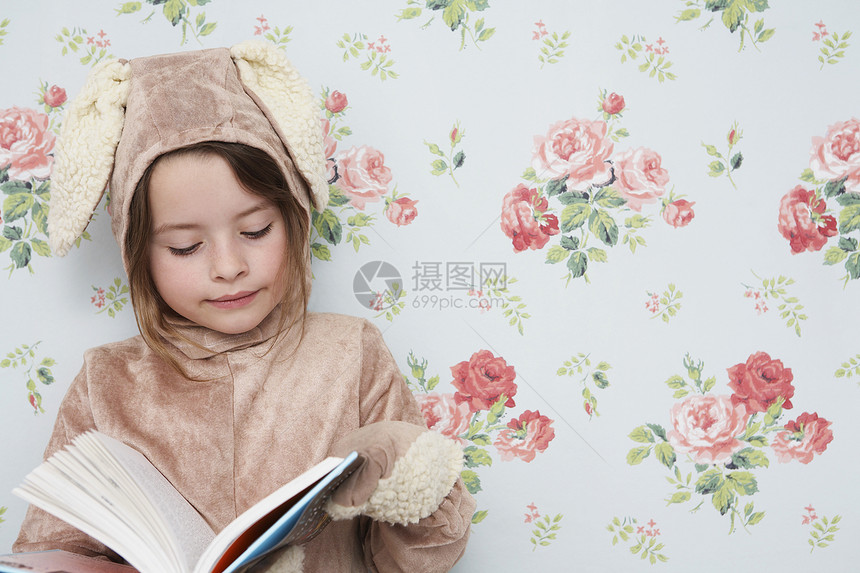 穿着兔子装扮的年轻女孩阅读书 与花粉型壁纸对立图片