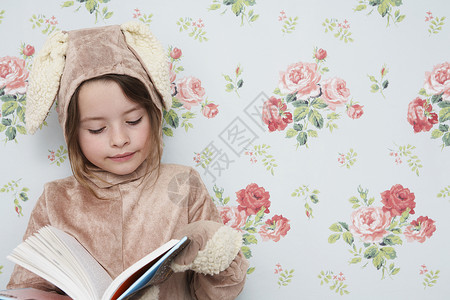 读书的兔子穿着兔子装扮的年轻女孩阅读书 与花粉型壁纸对立背景