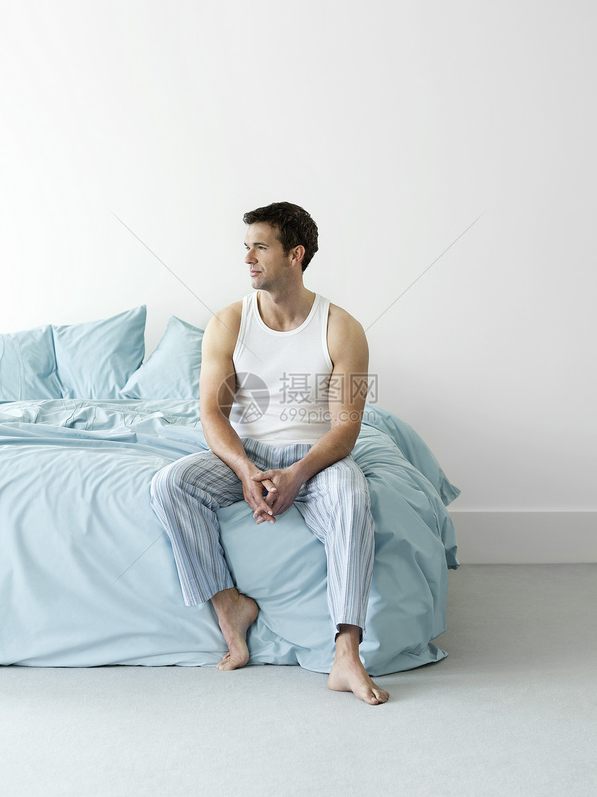 一个穿着睡衣 坐在床上的深思熟虑的年轻男子图片