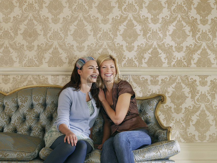 坐在沙地上和墙纸对着墙纸坐着的两位快乐的年轻女性图片