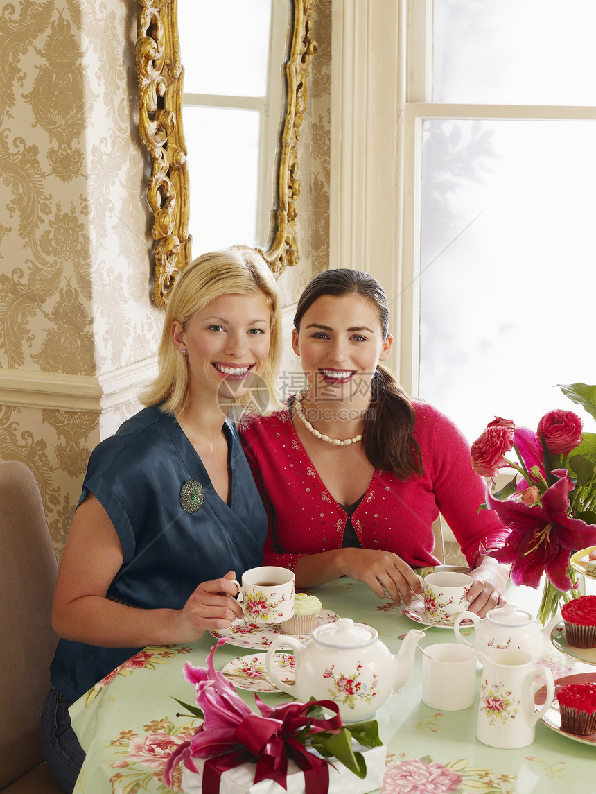 两个微笑的年轻女子在餐桌上喝茶的肖像快乐古董房间茶壶展柜花朵公寓花瓶女性成人图片