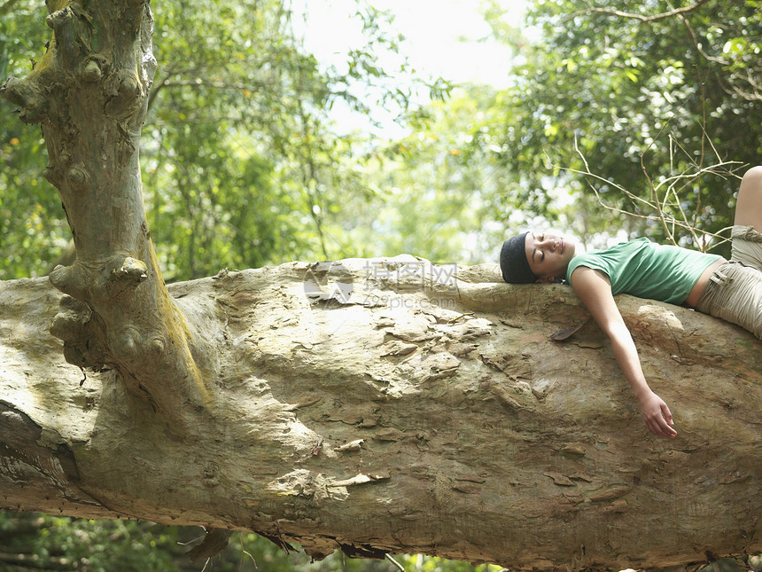 一位年轻混合种族女子的侧面景象 她躺在森林中的大树枝上女士女性旅行睡眠眼睛头巾树干游客勘探冒险图片