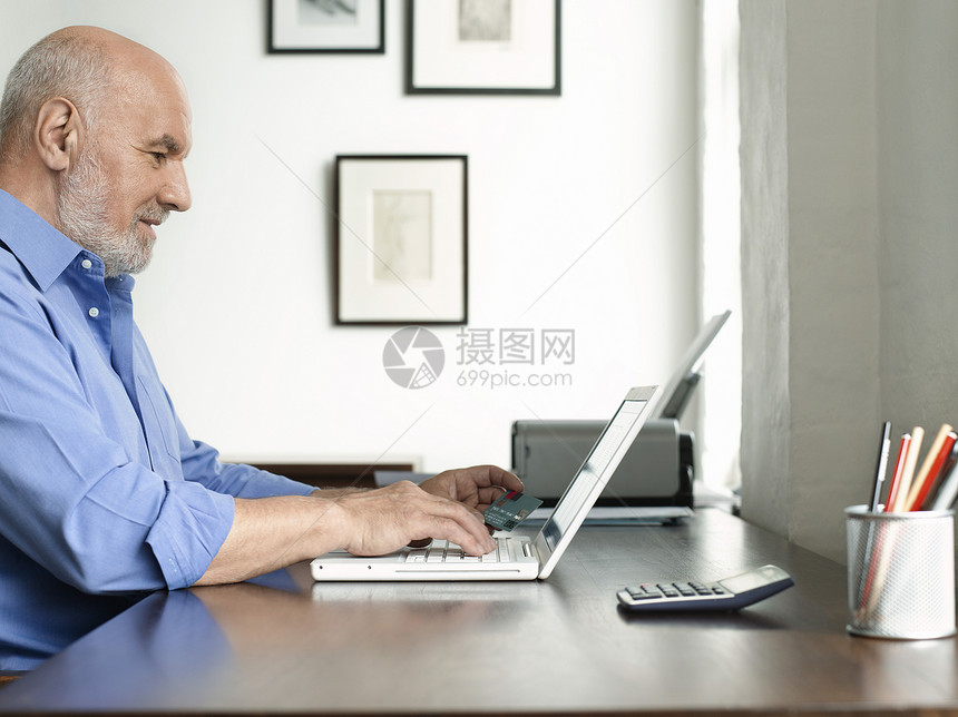 坐在办公桌上并使用笔记本电脑的成熟男子的侧面视图图片