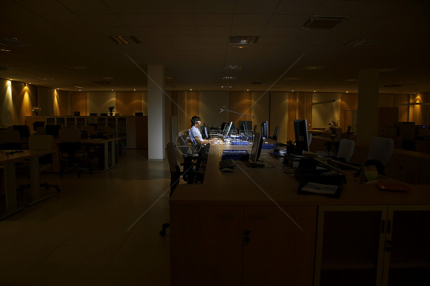 一位在暗办公室从事计算机工作的年轻女性的侧面视图专注房间商业黑暗监视器椅子中心职场女士桌面图片