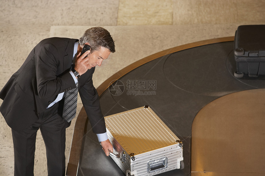 一名商务人士在机场行车行李上使用手机时 一整身的商务人士要求手提箱裁剪旅行婴儿乘客地面商业中年木马技术男人图片