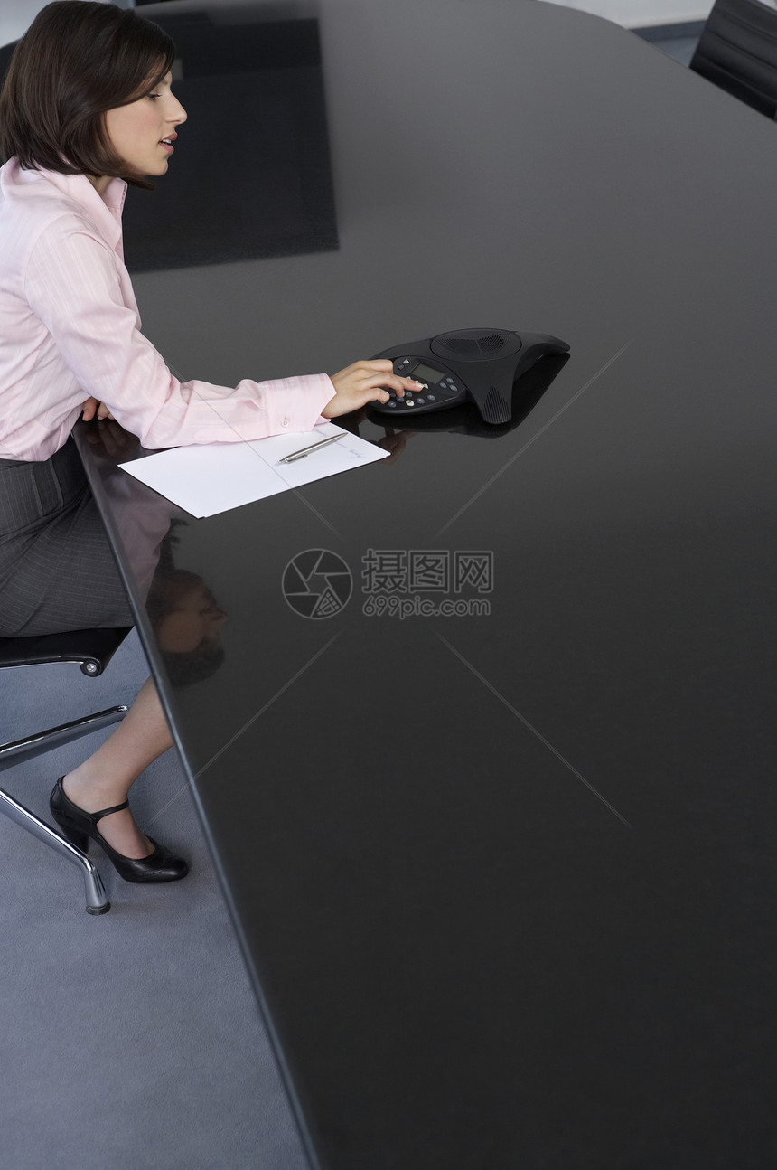 一位在会议桌上使用计算器的年轻女商务人士的侧边视图图片