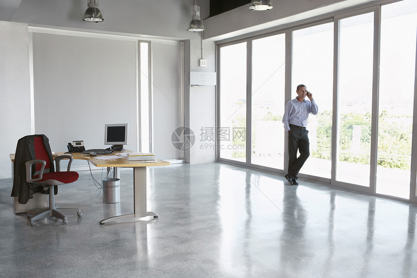 一名男性执行官在空办公室用手机对面玻璃墙顶着玻璃墙图片