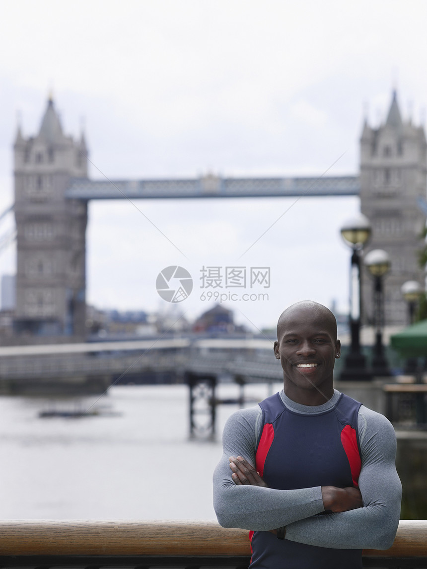 一个微笑着的年轻非裔美国人男子的肖像 手交叉在英格兰塔桥前穿过双臂图片