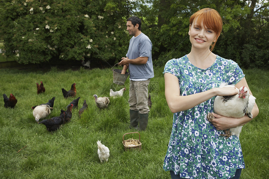 在草地喂养母鸡的年轻夫妇图片
