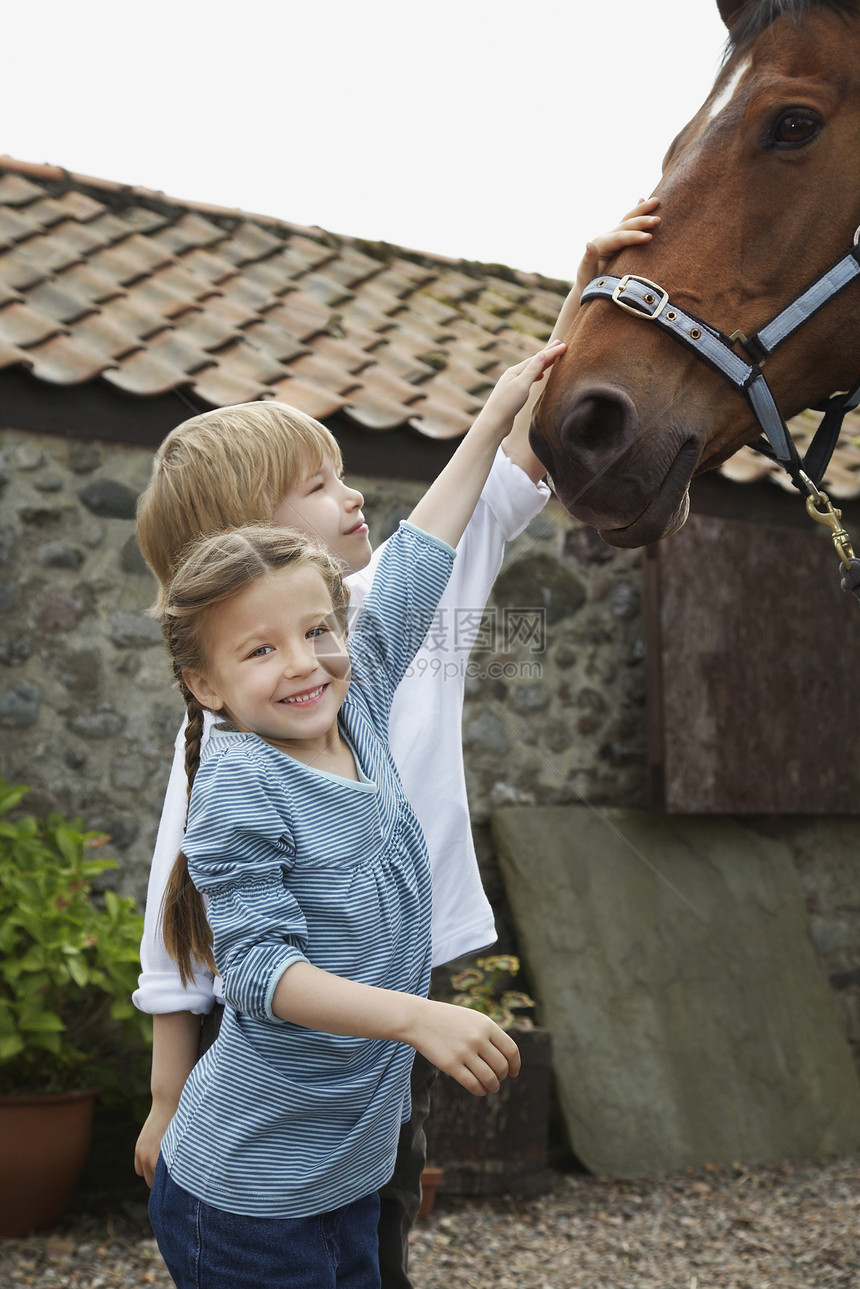 微笑的女孩和男孩在马棚外面打马图片