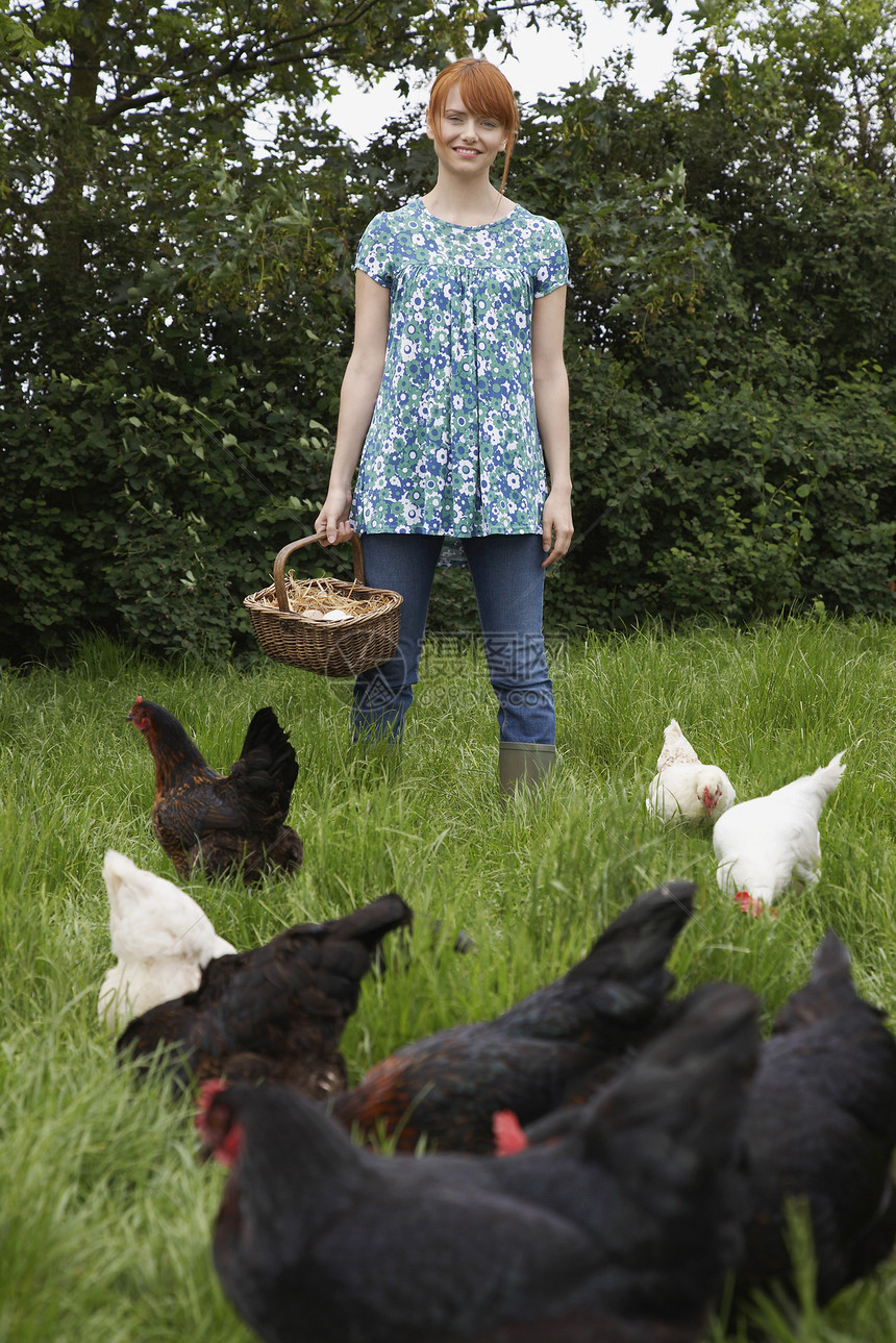 一个微笑的年轻女人的肖像 拿着鸡蛋篮在花园里图片