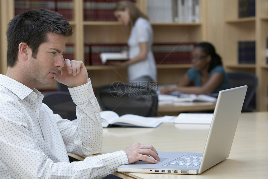 男性办公室工作人员使用手提笔记本电脑与女性同事在办公室背景的侧面视图图片