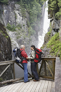 在瀑布附近的一男一女的全长侧视线 互相看着对方高清图片