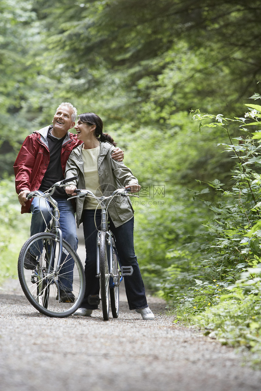 快乐的成熟男人和中年女人在林路上骑自行车图片