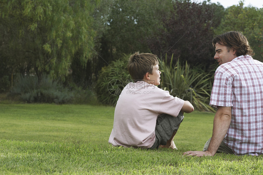 父亲和儿子坐在草坪上聊天的近视图片