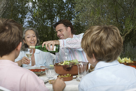 有孩子的家庭在花园里吃饭 当男人把酒倒入玻璃杯时高清图片