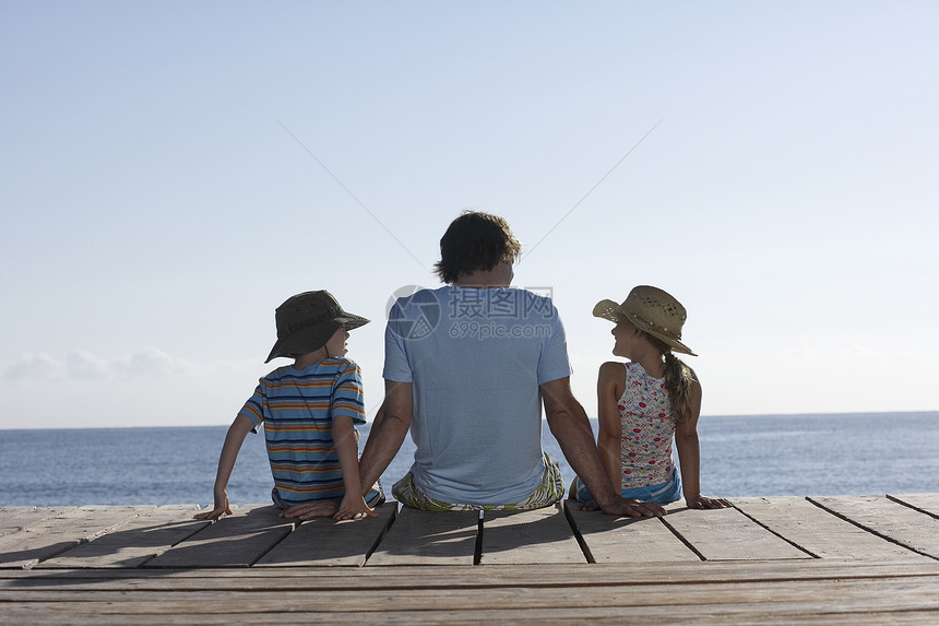 看见一个坐在码头上有两个孩子的男人的近视闲暇帽子女儿家长姐姐孩子们天空儿子女孩团结图片