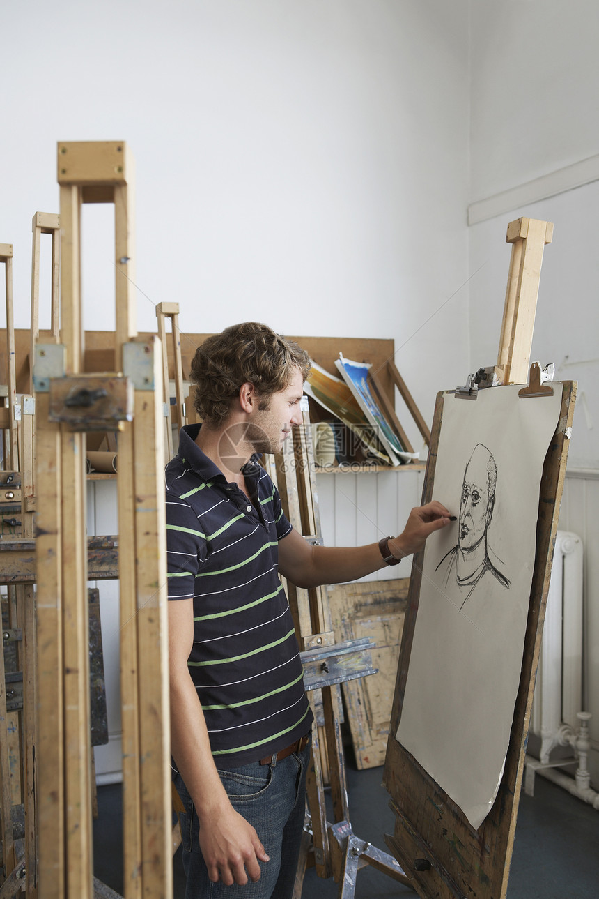一个男性艺术家在演播室画木炭肖像的侧景木头专注绘画深色工作室男人艺术画架大学微笑图片