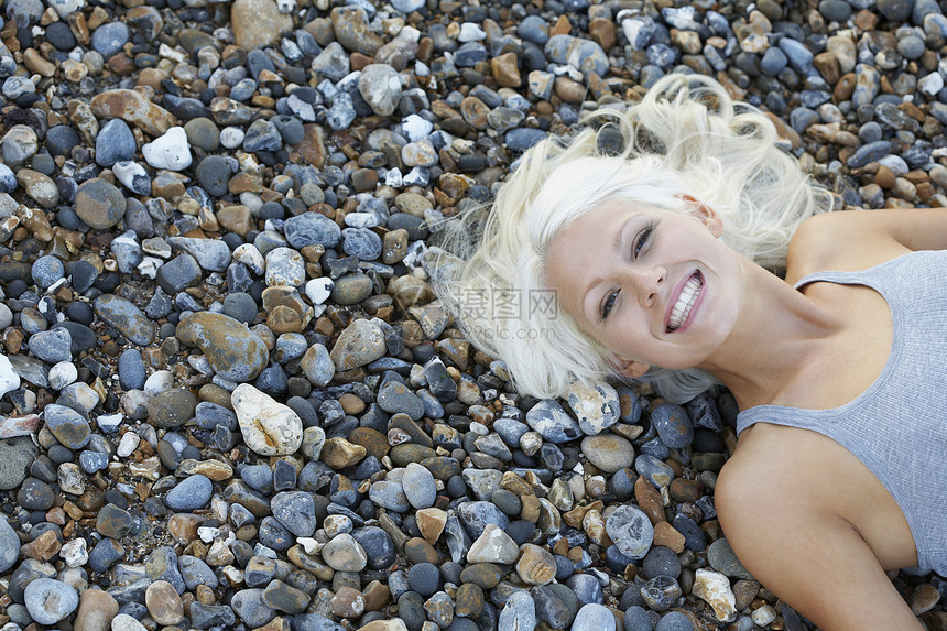 年轻女子在从上到下躺在沙滩的石子景色上微笑图片