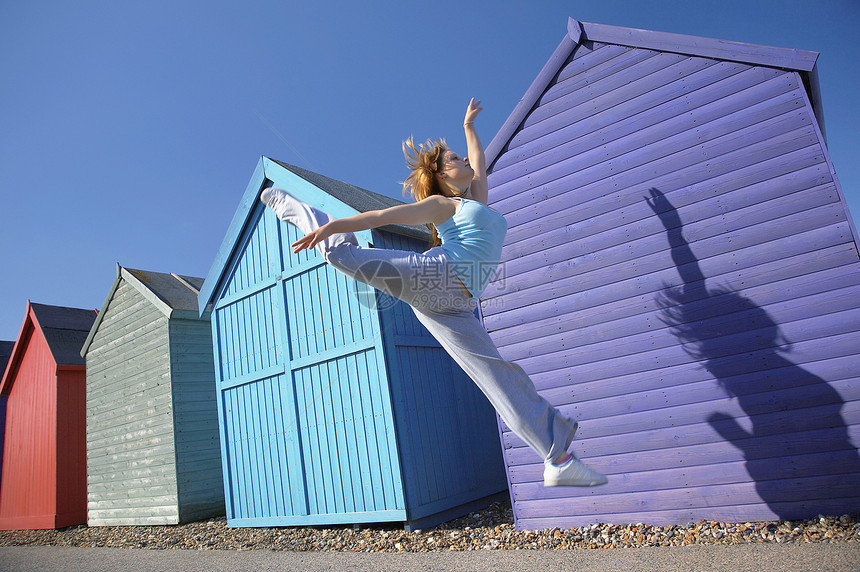 女人在海滩小屋前跳跃成年休闲杂技行动双腿视图运动成人服装低角度图片
