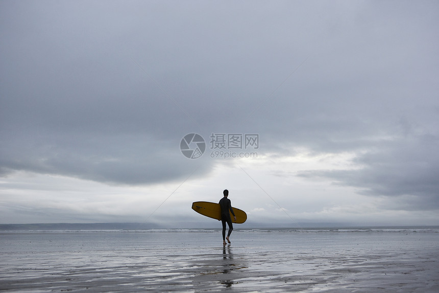在海滩后视线上携带冲浪板的Surfer图片