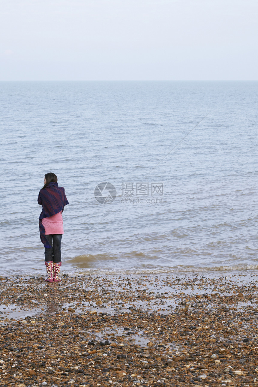 围着毯子的年轻女性近视 在海滩上海边站立图片