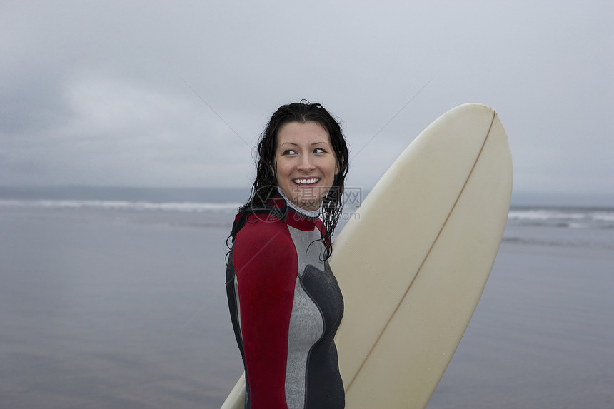 快乐的女性冲浪者的侧面景色 与冲浪板看远海滩图片