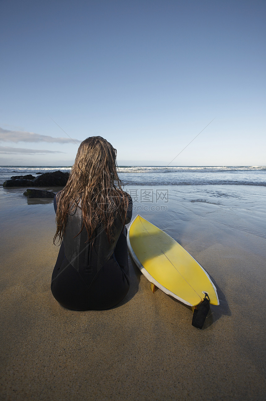 坐在海滩上冲浪板边的年轻女子的近视图片