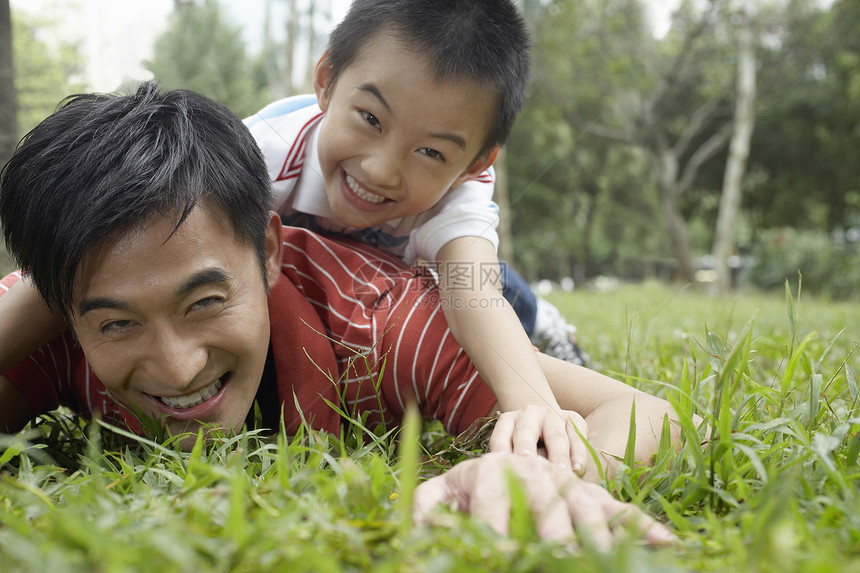快乐的父亲和儿子躺在公园的草地上图片